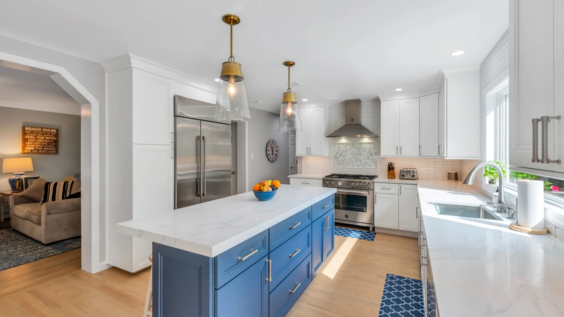 A bright white kitchen features a blue island and stainless steel appliances.