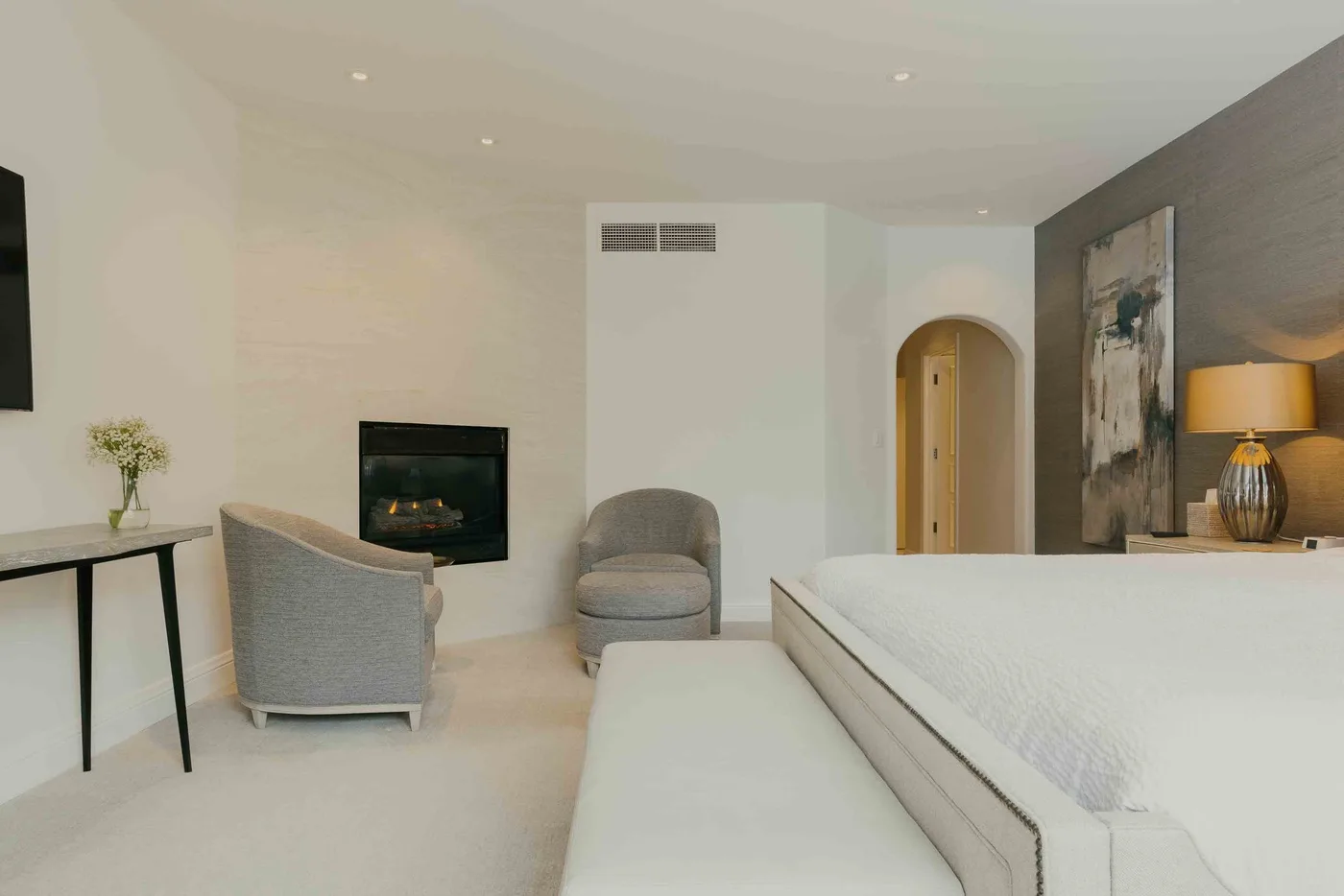 A bright bedroom with a fireplace, seating, and a bed.