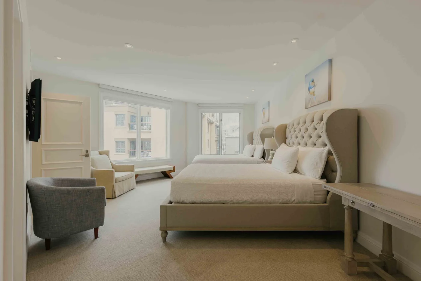A bright bedroom with a large bed and windows overlooking nearby buildings.