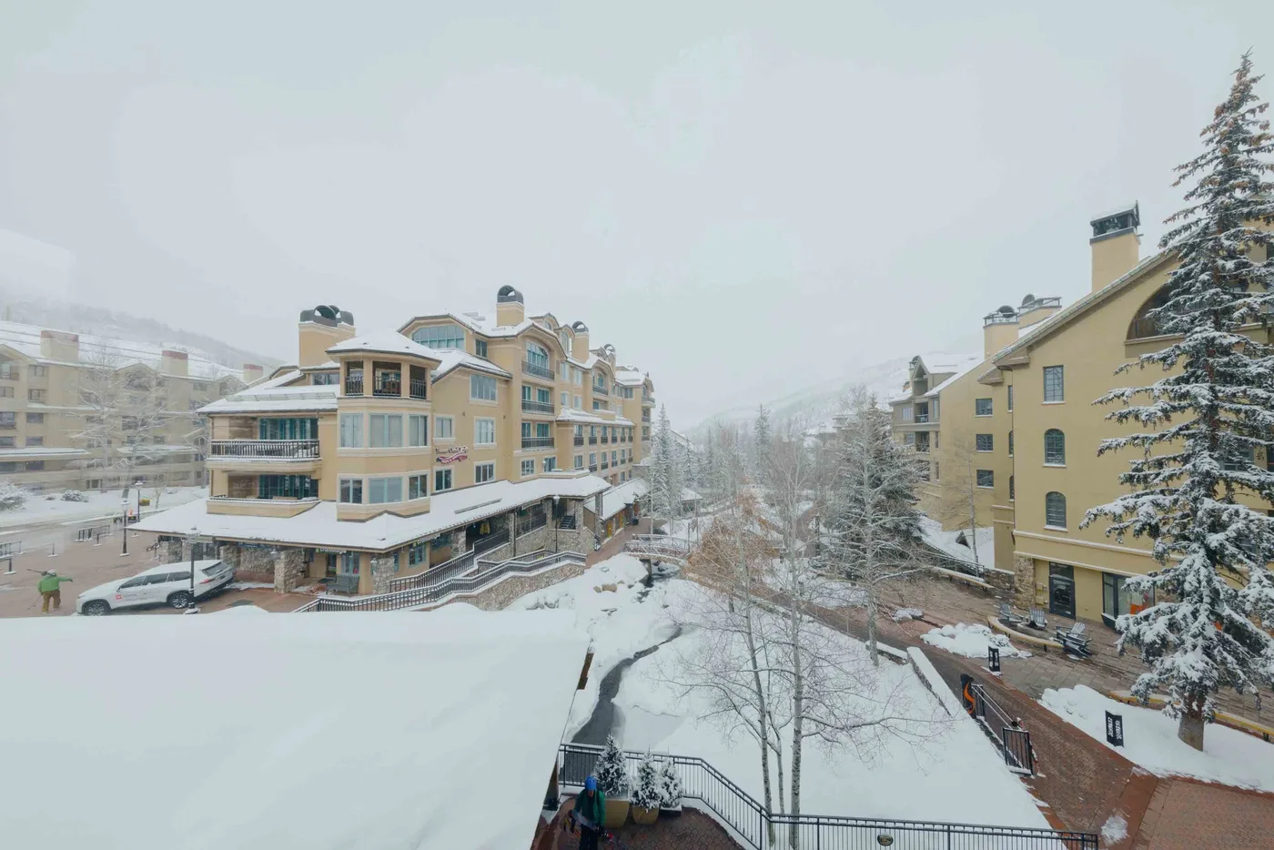 Snow-covered hotel buildings surround a courtyard with bare trees and a walkway.