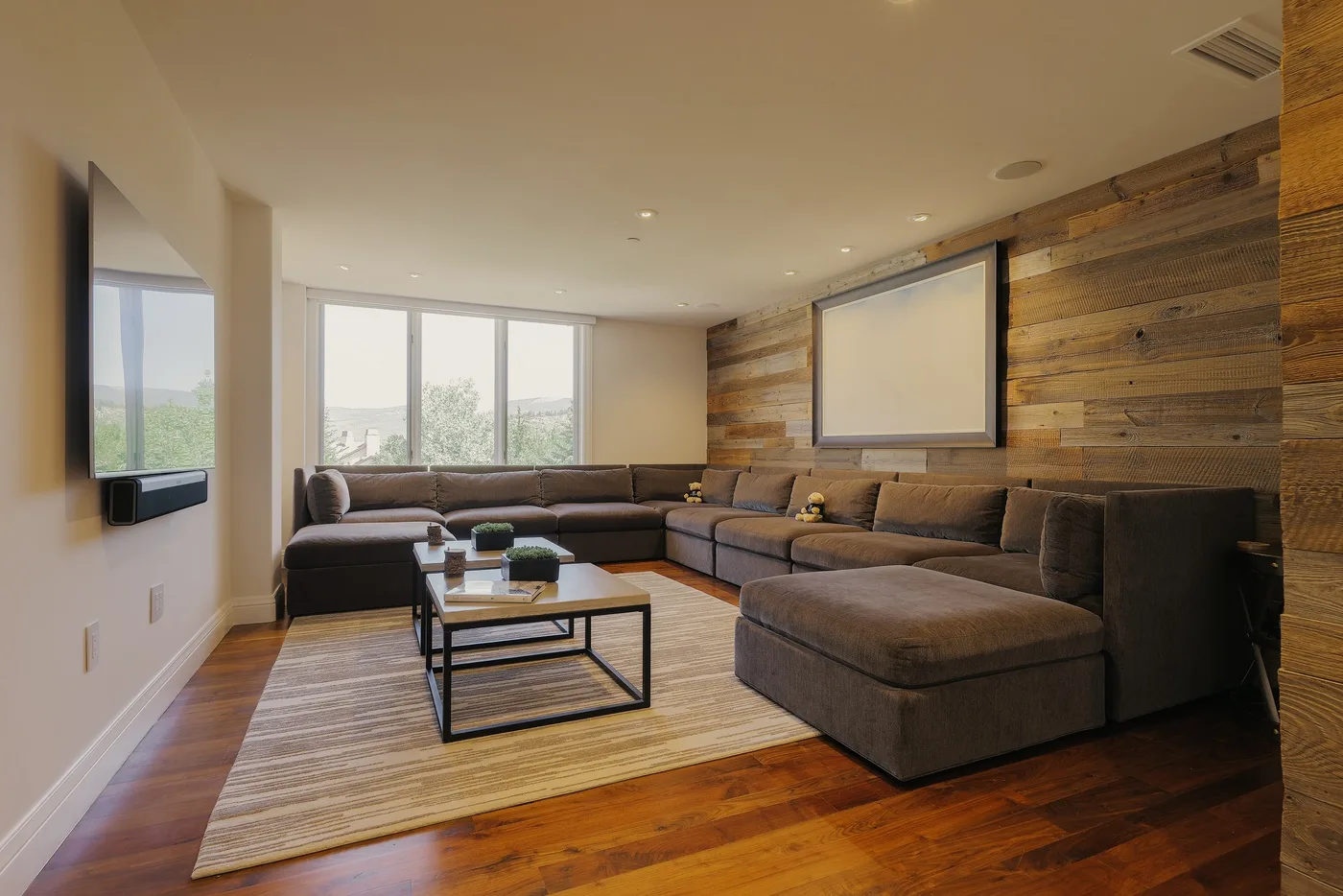 A living room with sectional seating, a large rug, and a wall-mounted screen.