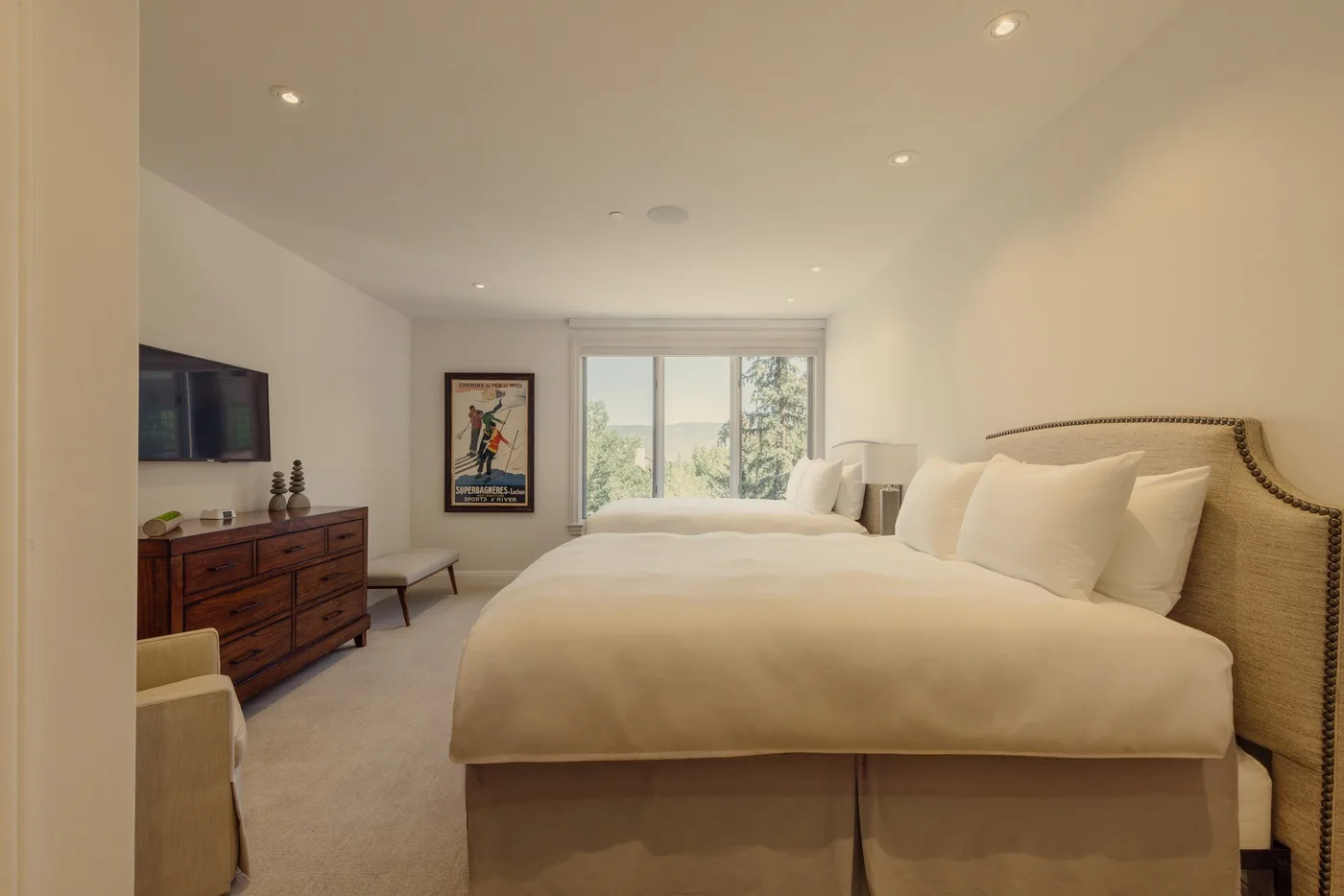 A bright bedroom with a large bed, a window, and a dresser.