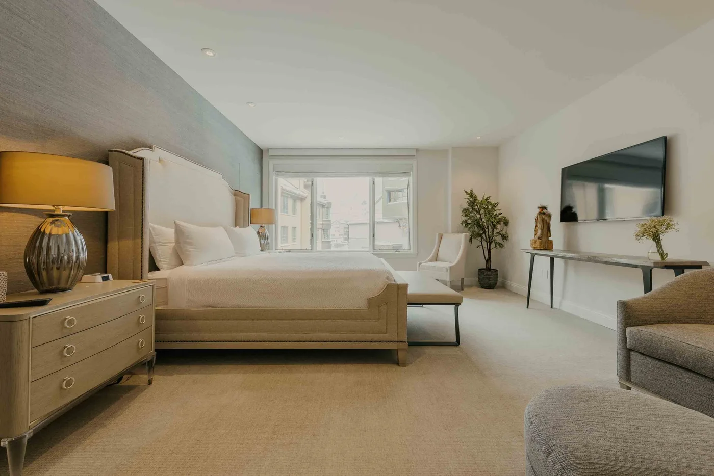 A bright bedroom with a bed, seating, and a large window.