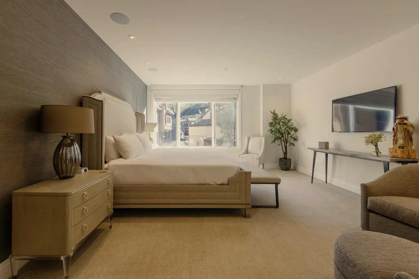A bright bedroom with a bed, a large window, and seating.