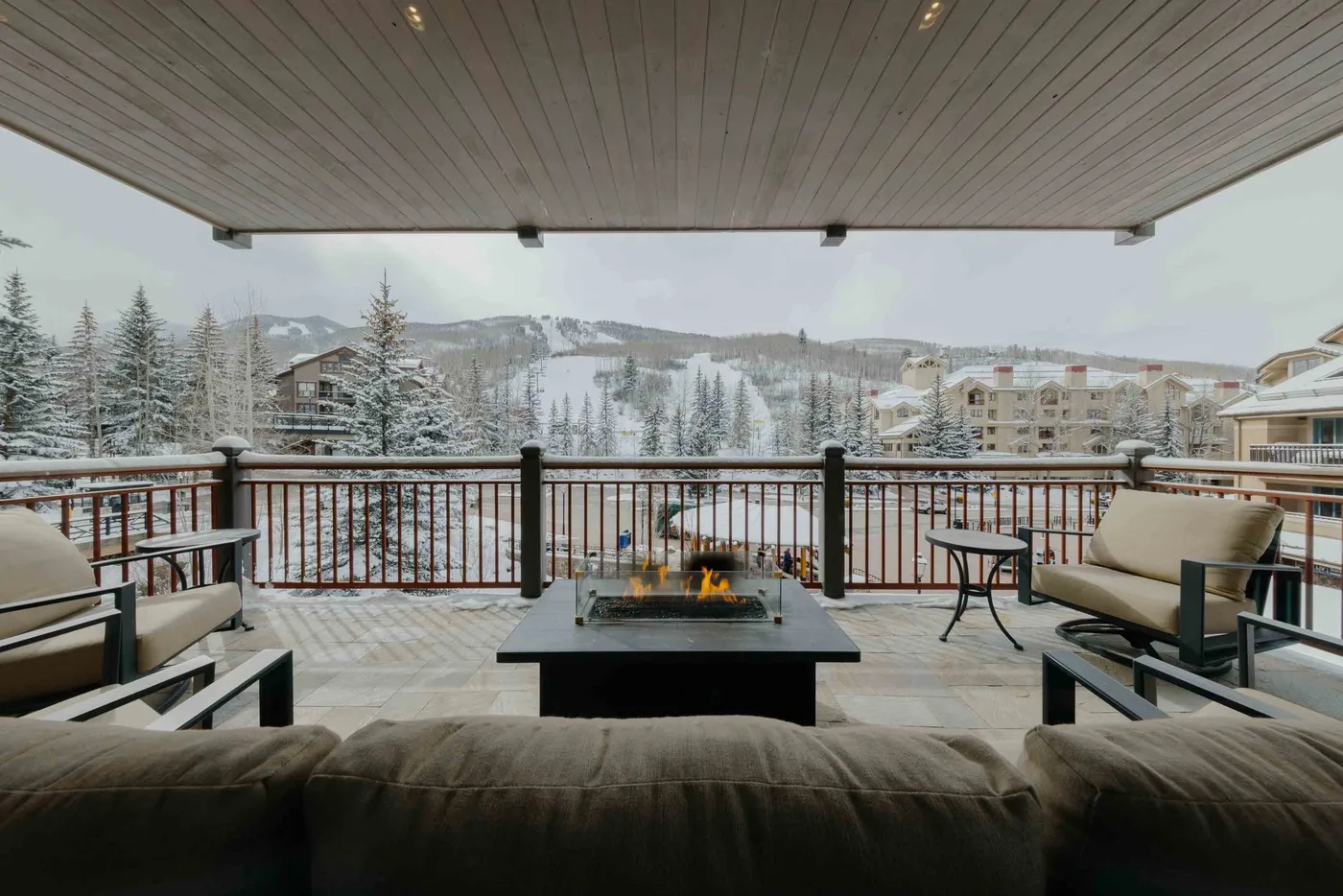 A covered outdoor seating area overlooks a snowy landscape, with a fire table in the center.
