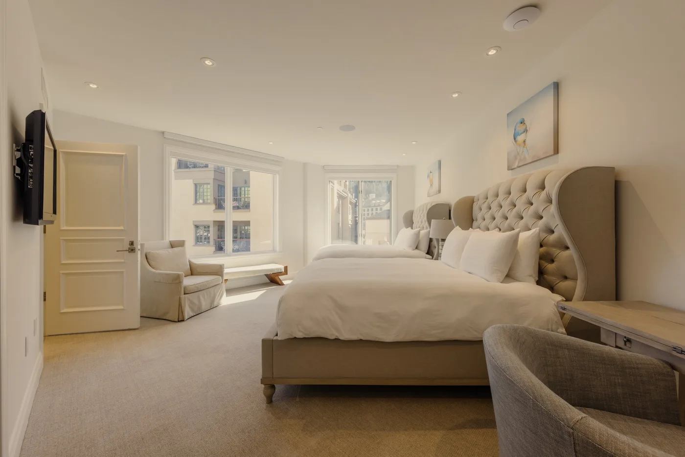 A bright bedroom with a large bed, armchairs, and wide windows.