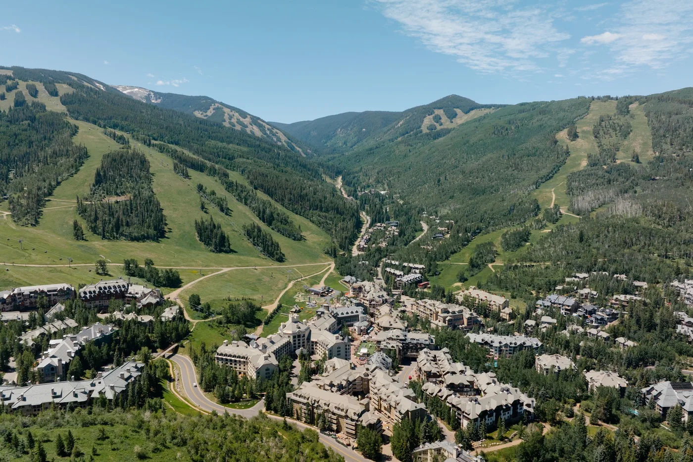 A mountain valley with a town nestled among green slopes beneath a blue sky.