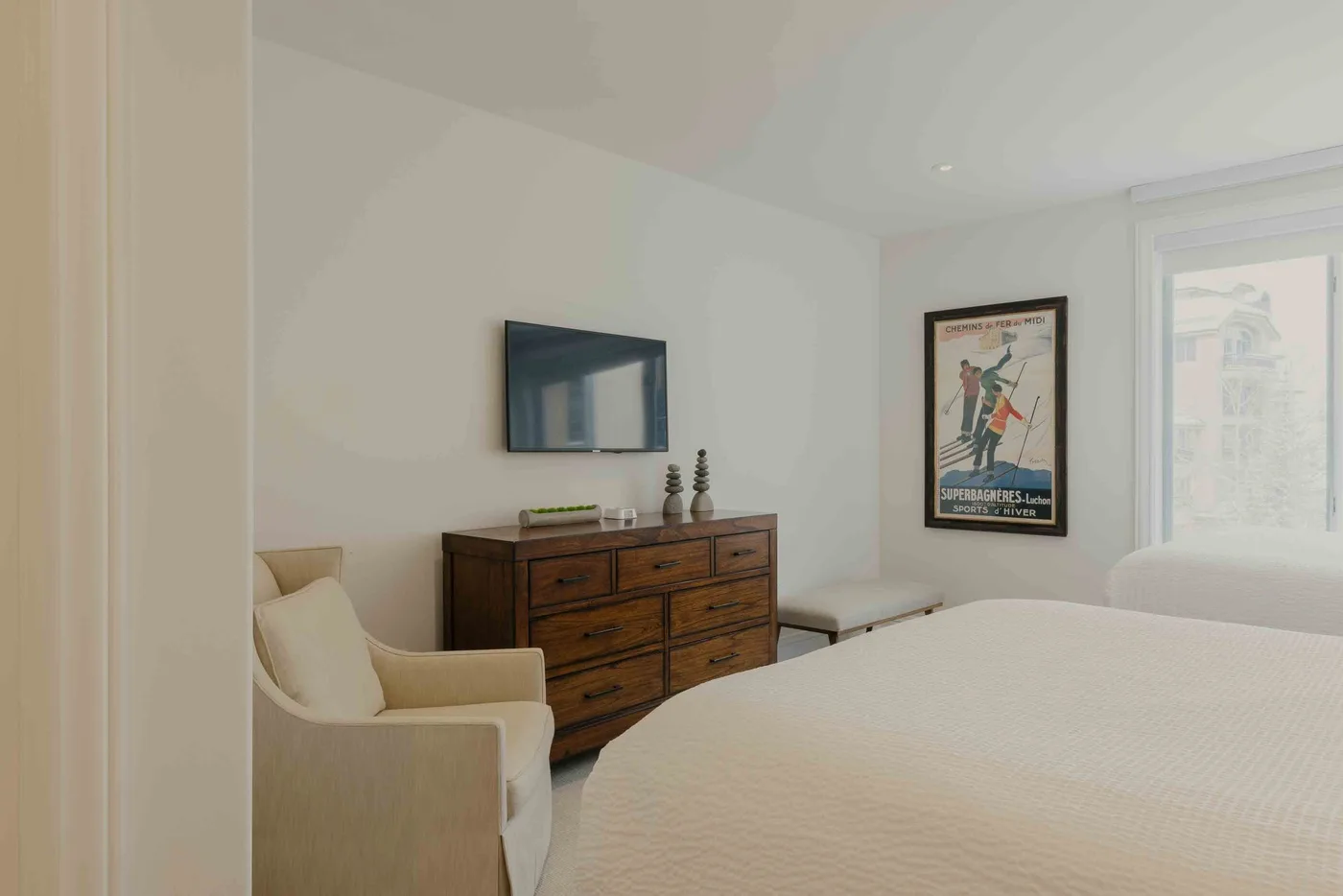 A bright bedroom with a bed, upholstered seating, and a wooden dresser.