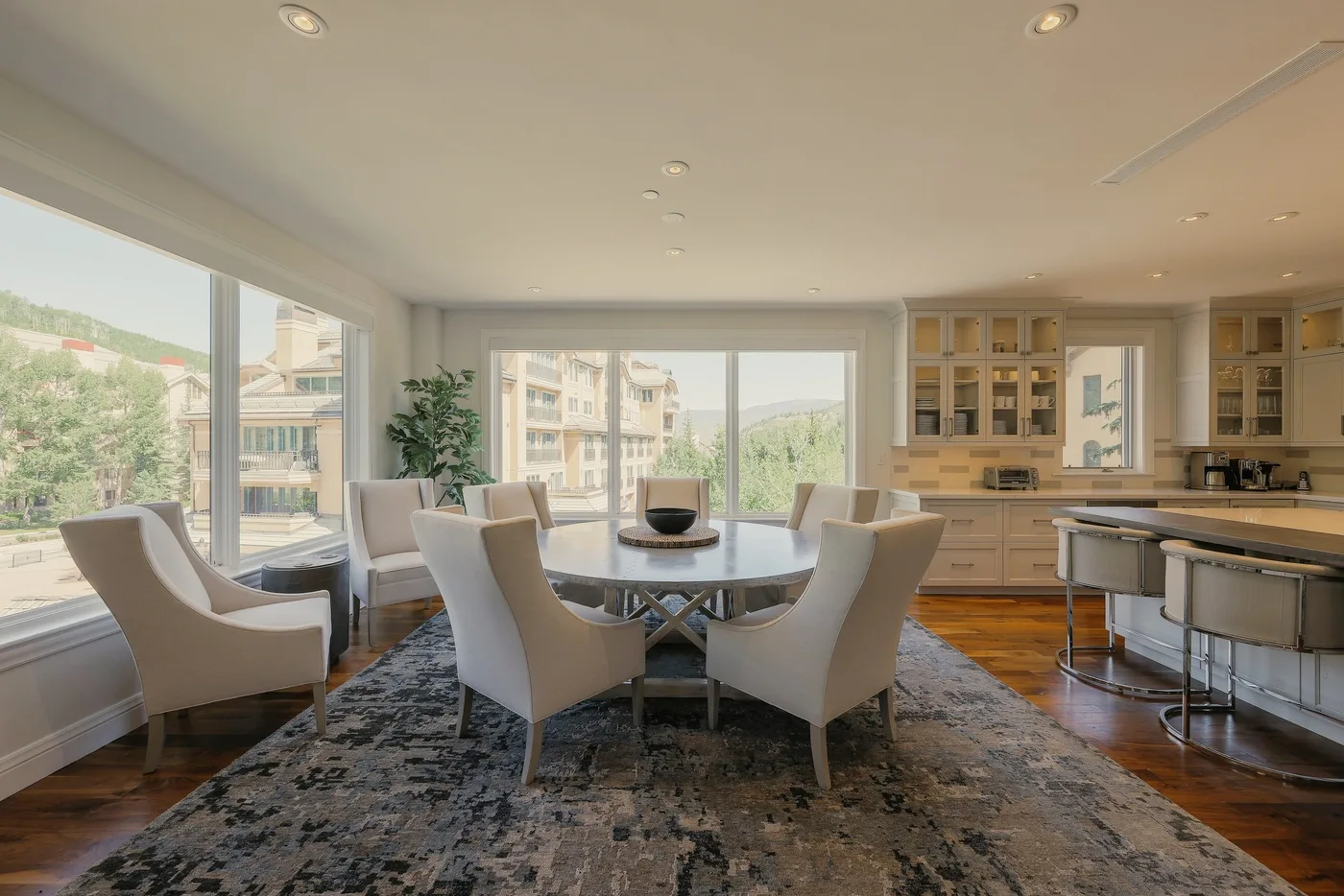 A bright dining area with a round table and large windows overlooking nearby buildings.