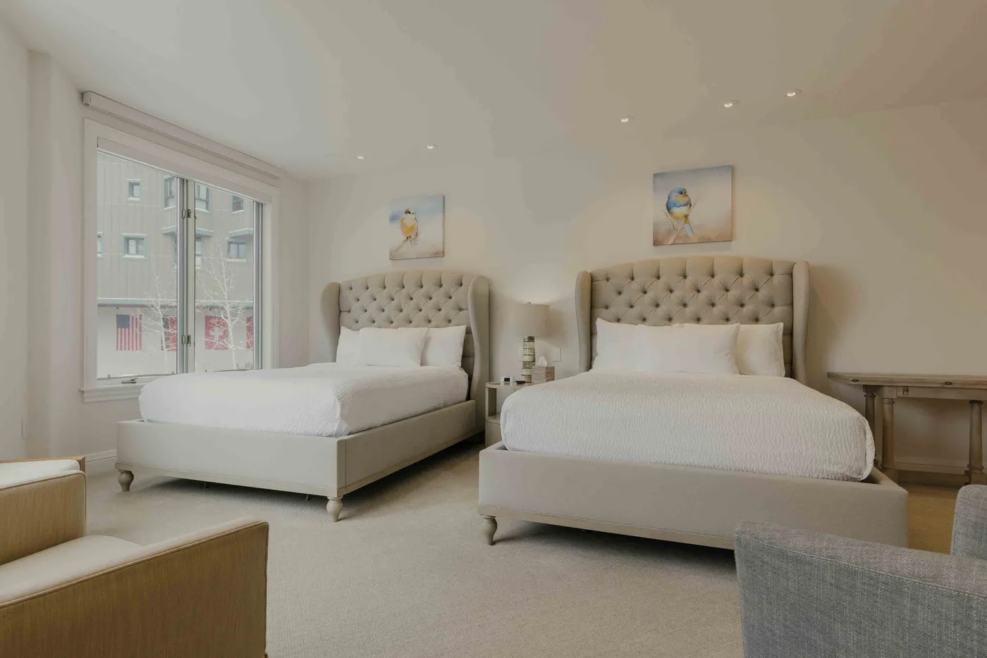 A bright bedroom with two beds, bedside tables, and a large window.