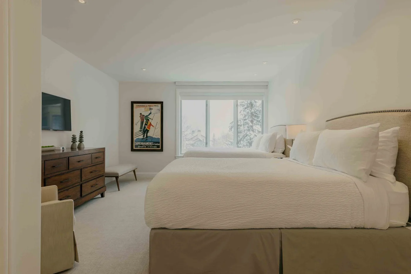 A bright bedroom with a neatly made bed, a dresser, and a large window.