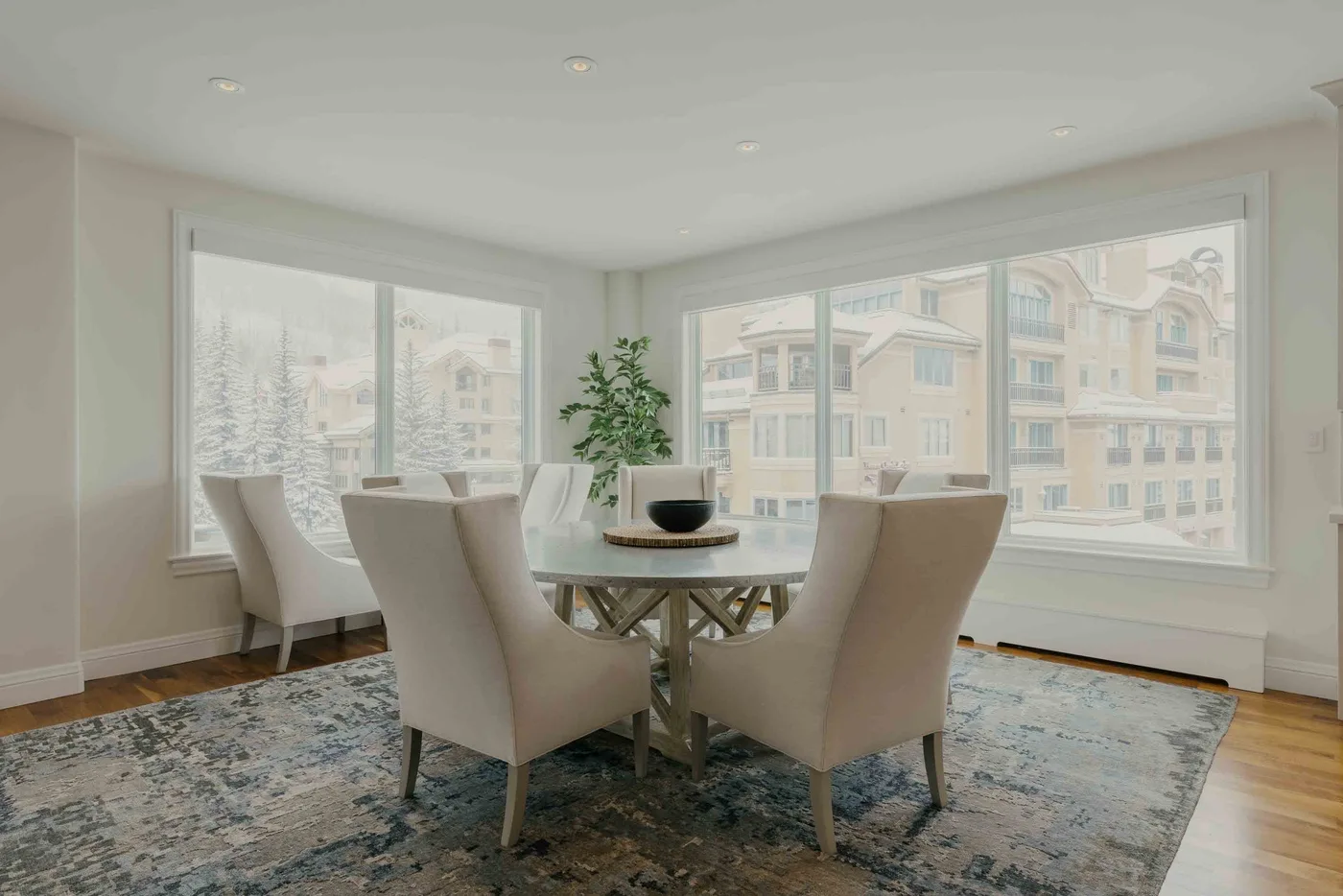 A dining area with upholstered seating around a table beside large windows.