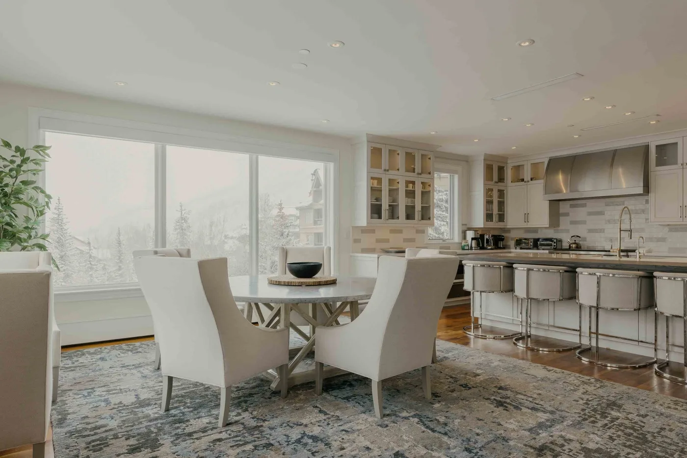 A bright dining area opens onto a kitchen, with large windows and a dining table.