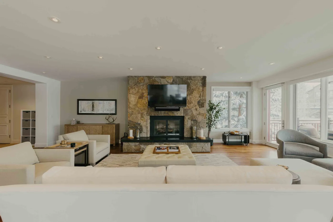 A bright living room with seating arranged around a stone fireplace and television.