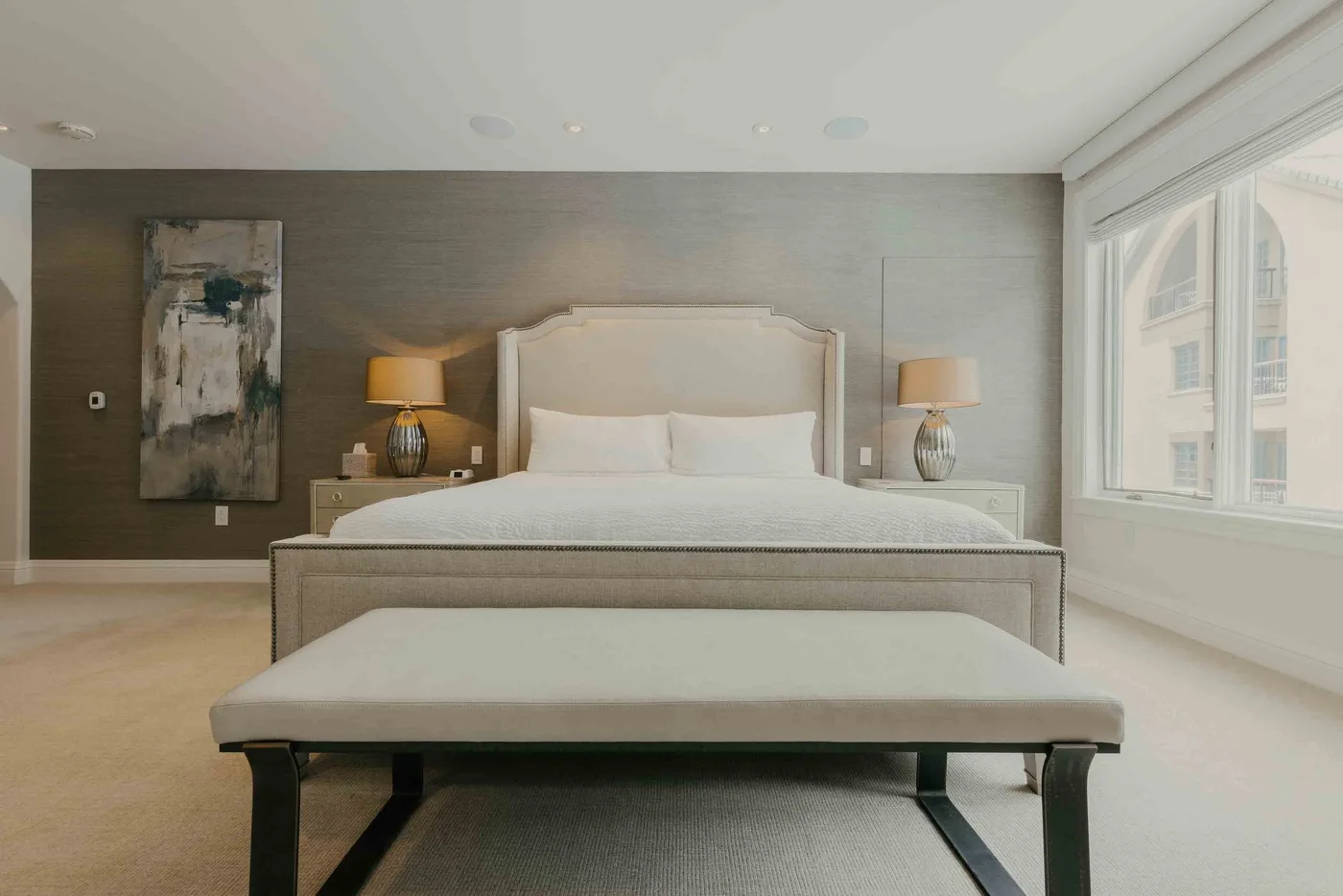 A bedroom with a large bed, matching bedside lamps, and a bench at the foot.