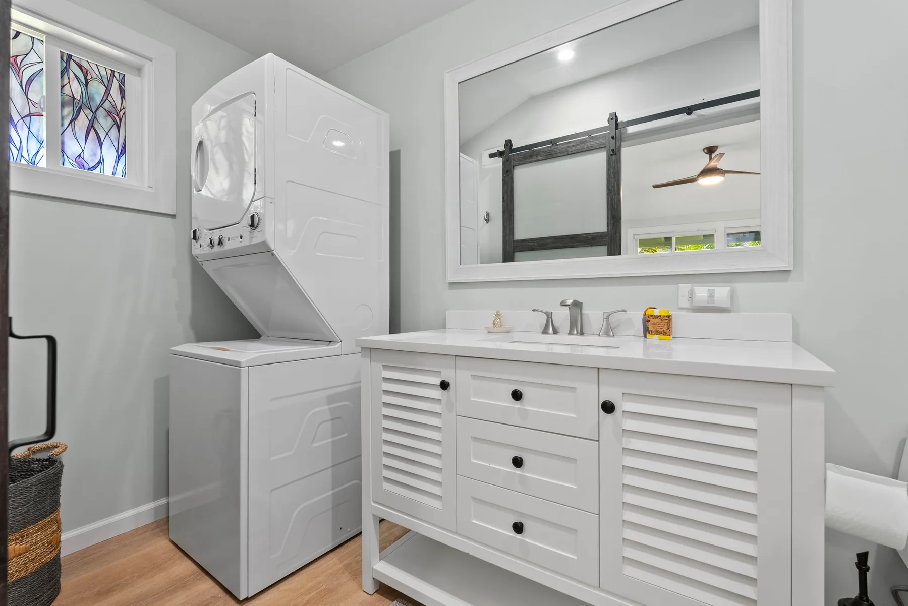 Un tocador de baño luminoso con un espejo grande está junto a una lavadora y secadora apiladas.