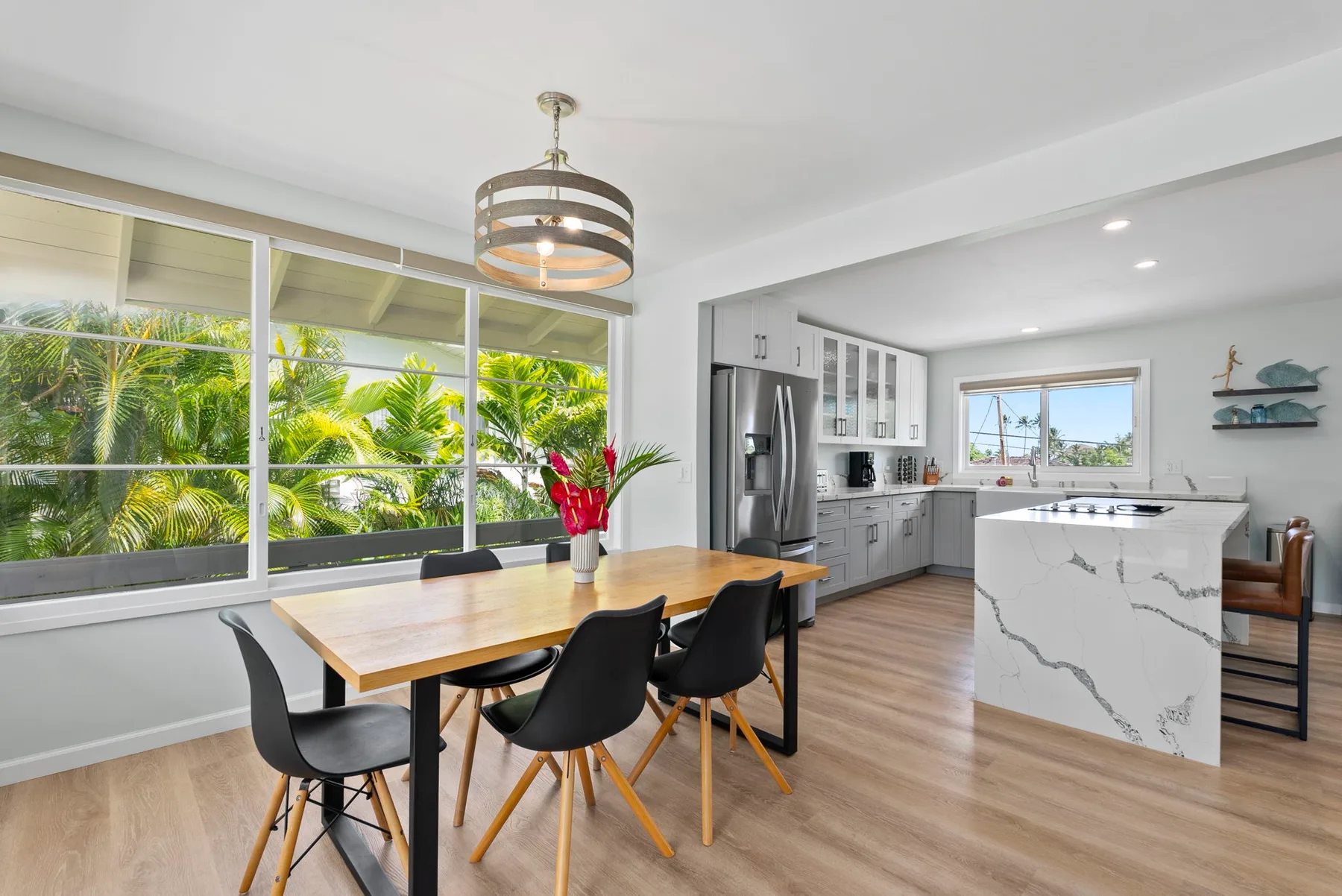 Una cocina abierta con comedor tiene una mesa de madera junto a grandes ventanas.