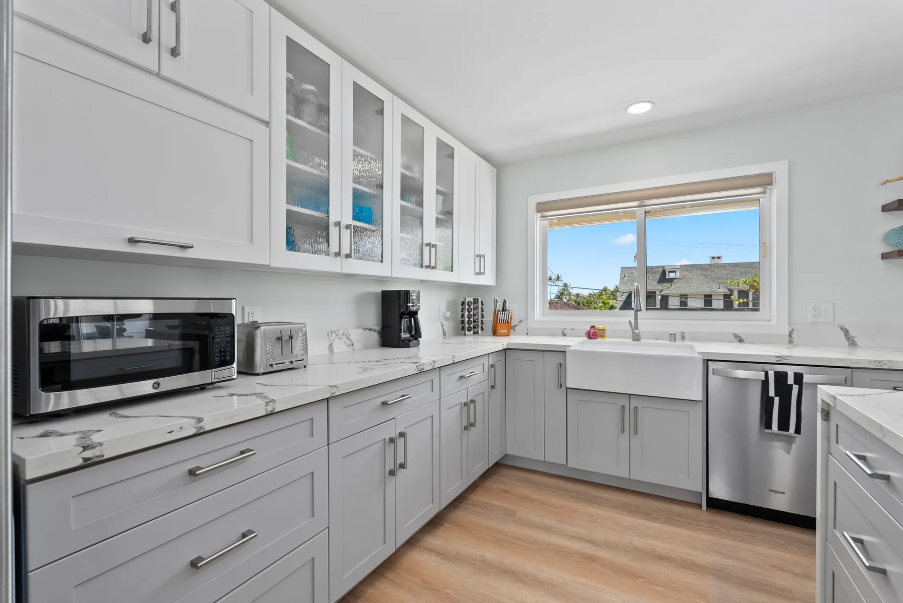 Una cocina luminosa con gabinetes blancos, una encimera y una ventana con vista a los tejados.