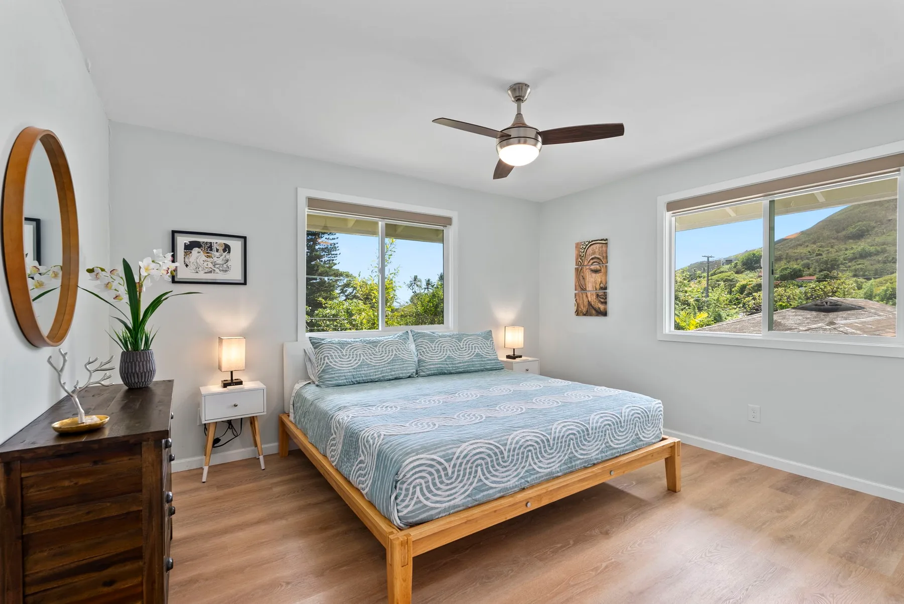 Un dormitorio luminoso con una cama entre dos ventanas con vistas a colinas verdes.