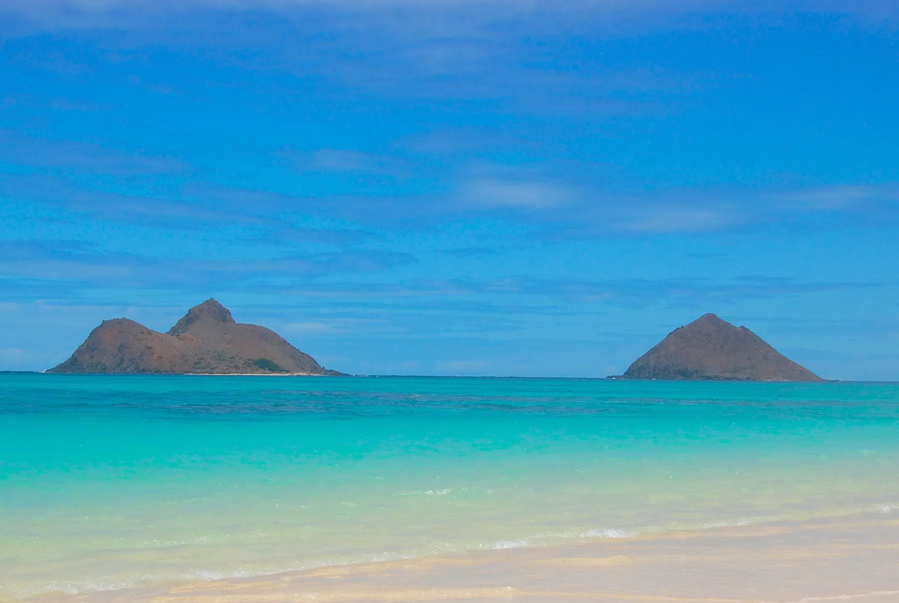 Una playa tropical con agua turquesa y dos islas en el horizonte.
