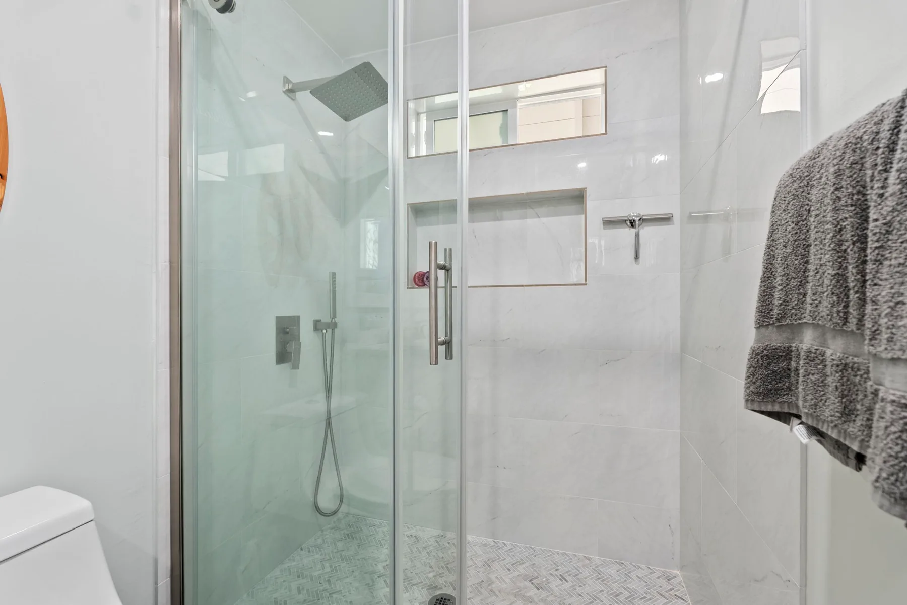 Un baño luminoso con azulejos, una ducha de vidrio y toallas colgadas.