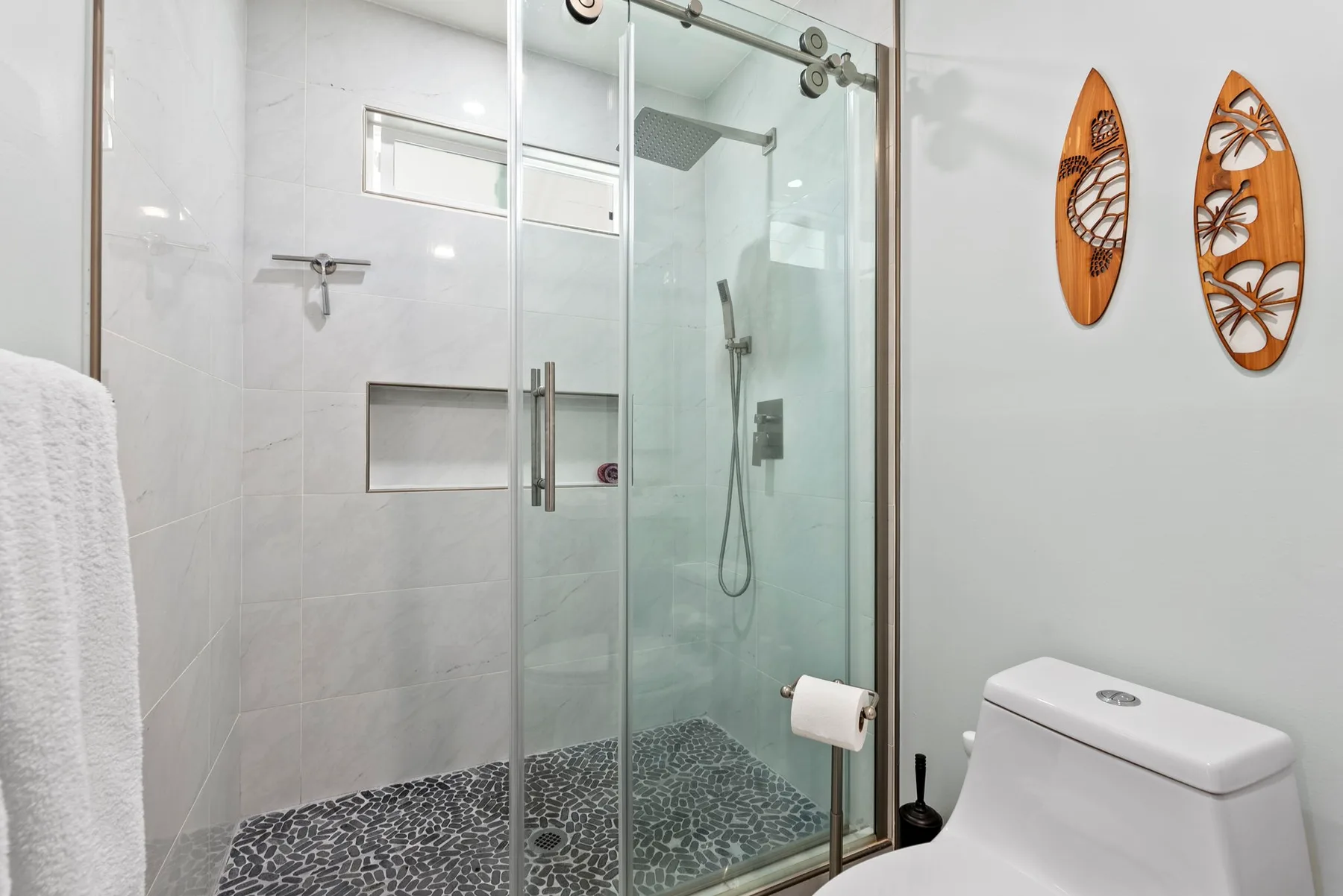 Un baño con una ducha de vidrio y un inodoro junto al área alicatada.
