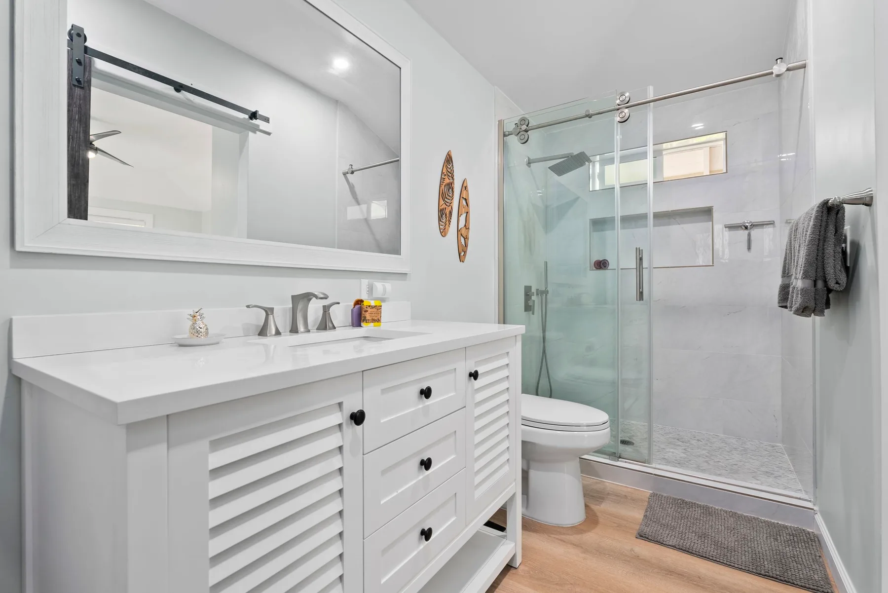 Un baño luminoso con un tocador blanco, espejo y ducha de vidrio.