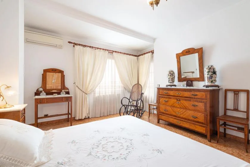 A bright bedroom with a large bed, curtained window, and wooden furniture.