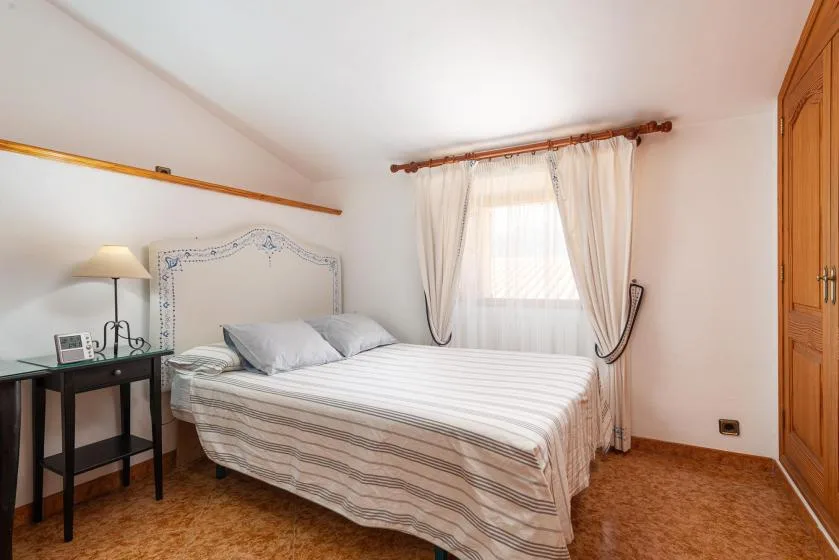 A bedroom with a bed, a curtained window, and a bedside table.