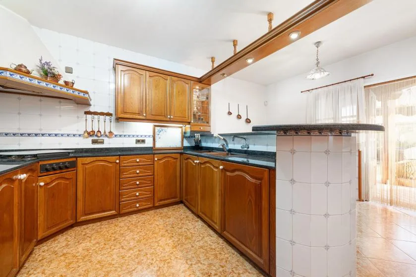 A bright kitchen with wooden cabinets, dark countertops, and a central tiled counter.