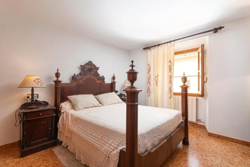 A bedroom with a carved wooden bed and a sunlit window.
