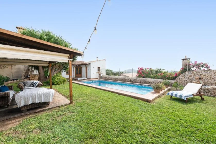 A garden patio overlooks a swimming pool, with shaded seating and a lounge chair.