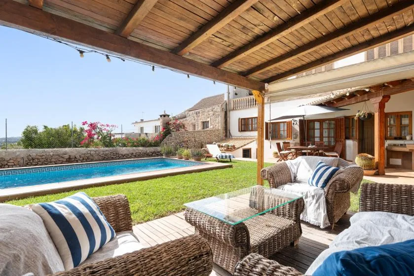 A covered patio with seating overlooks a lawn and swimming pool.
