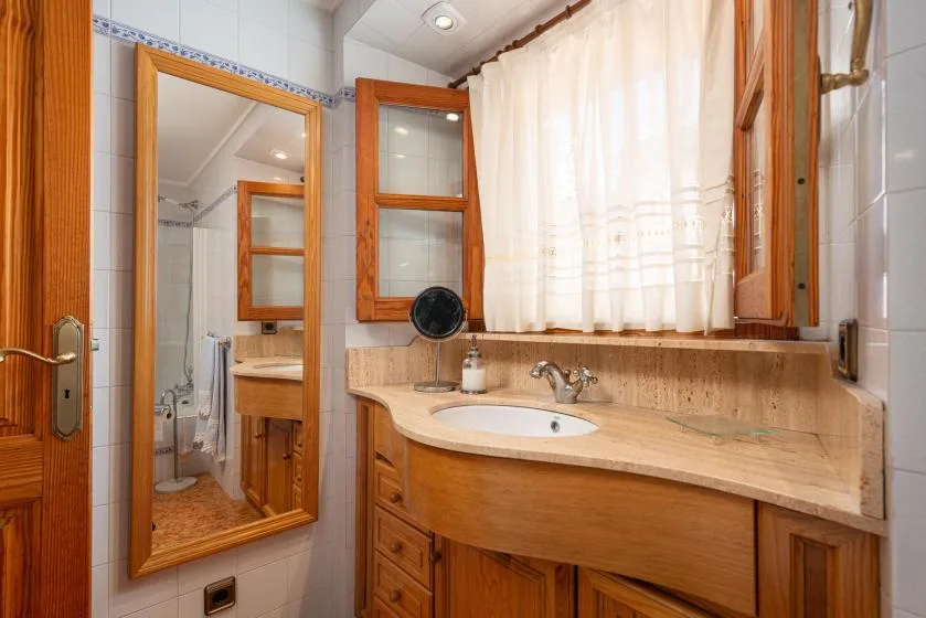A tiled bathroom with a wooden vanity, sink, and curtained window.