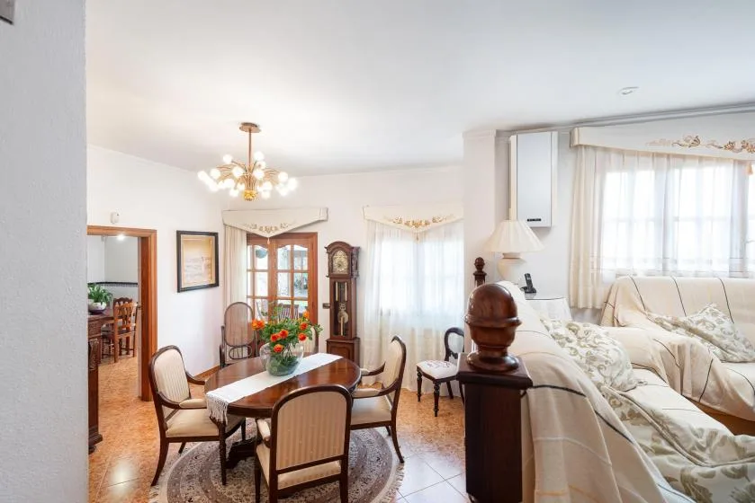 A bright dining area with a wooden table and chairs beside a living room.