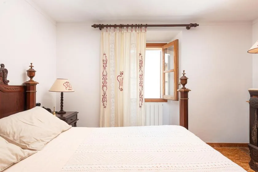 A bedroom with a bed and a curtained open window.