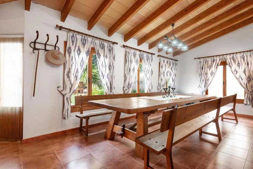 A dining room with a long wooden table and benches beneath exposed ceiling beams.