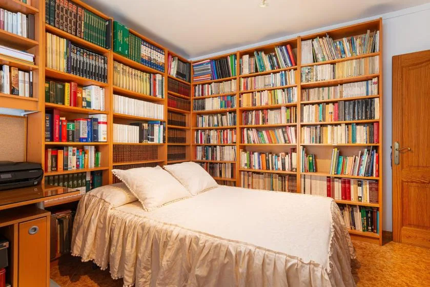 A bedroom with a bed in front of floor-to-ceiling bookshelves.