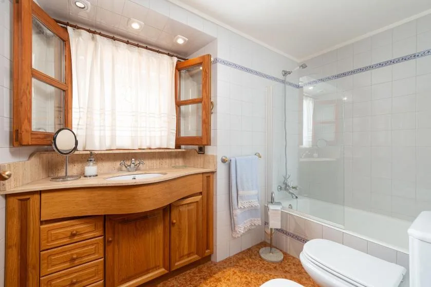 A tiled bathroom with a wooden vanity, bathtub, and toilet.