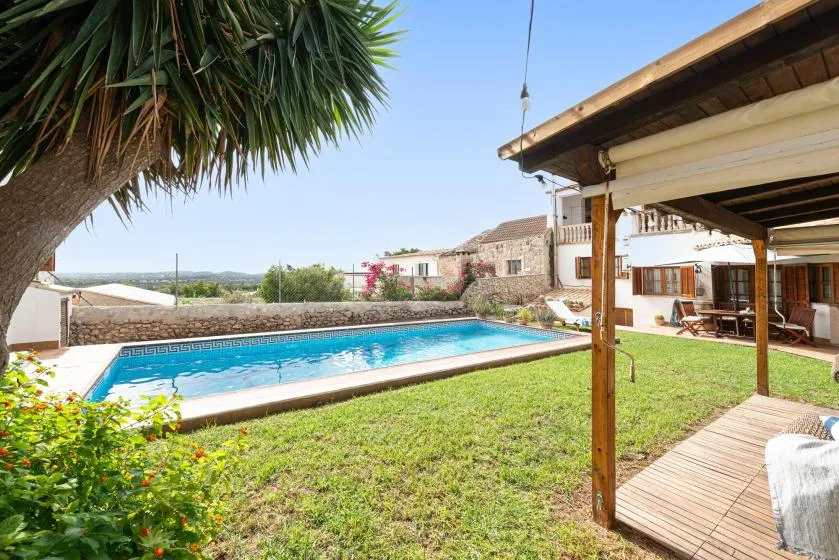 A garden patio overlooks a swimming pool beside a house.