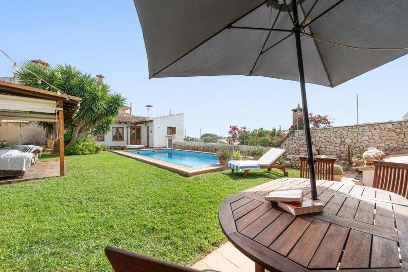 A garden patio with a swimming pool, lawn, and shaded outdoor seating.