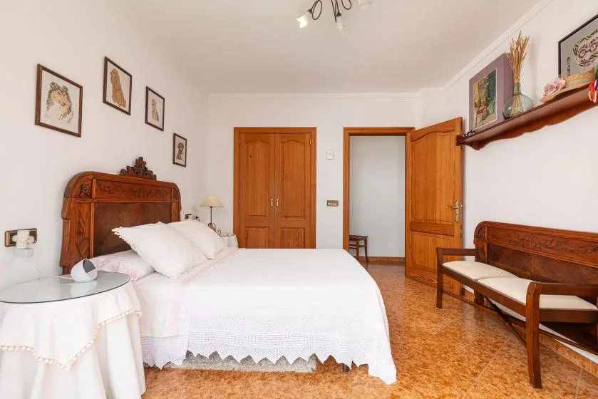 A bedroom with a white bed, wooden furniture, and framed pictures on the walls.