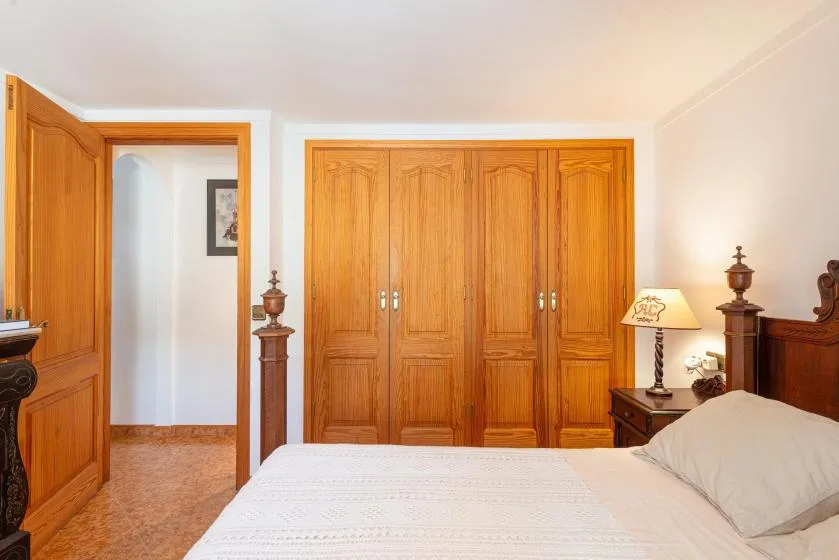 A bedroom with a bed in front of wooden wardrobes and an open doorway.