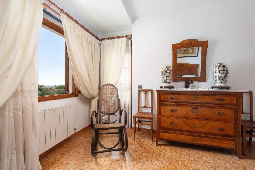 A bedroom with a wooden dresser, a rocking chair, and curtained windows.