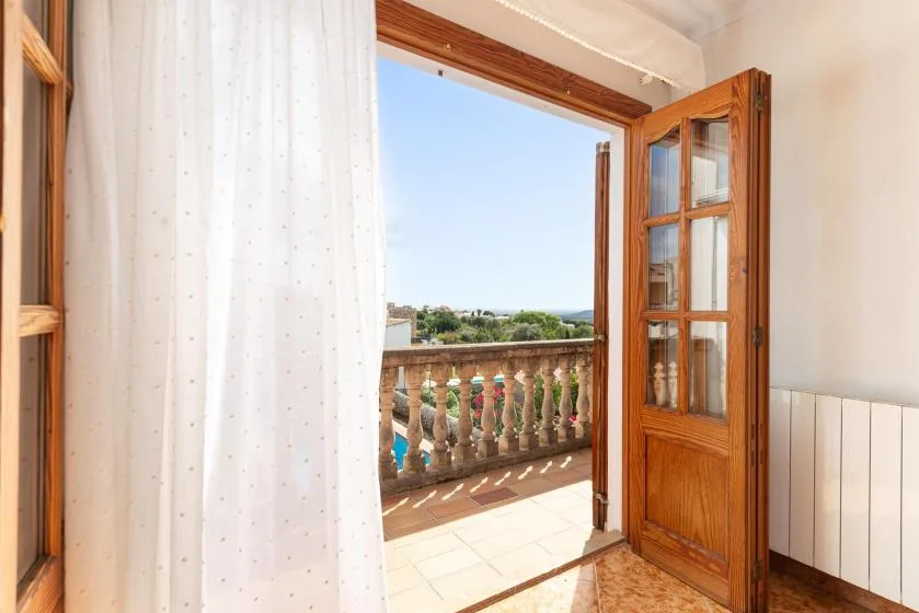 A bright room opens onto a balcony with a view of greenery and sky.