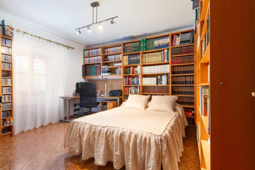A bedroom with a neatly made bed and bookshelves lining the walls.