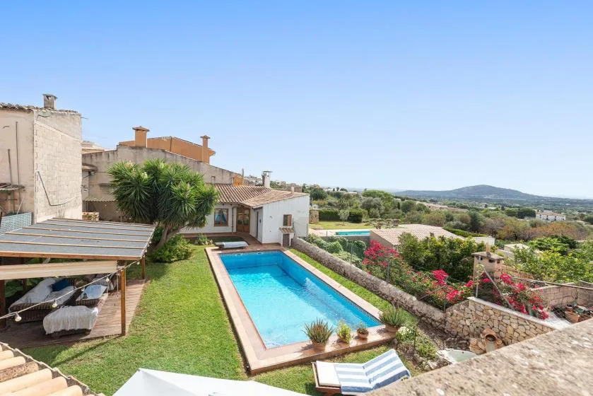 A garden swimming pool beside a house, with greenery and hills in the distance.