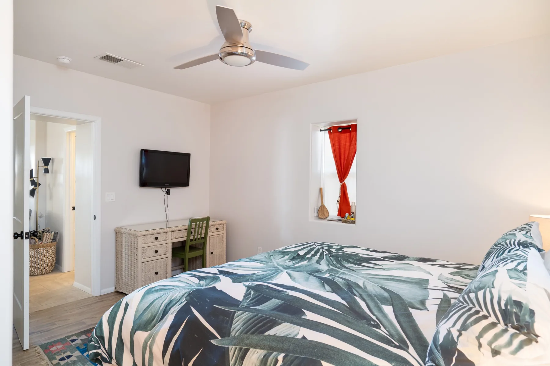 Un dormitorio luminoso con una cama, una cómoda y un televisor en la pared.