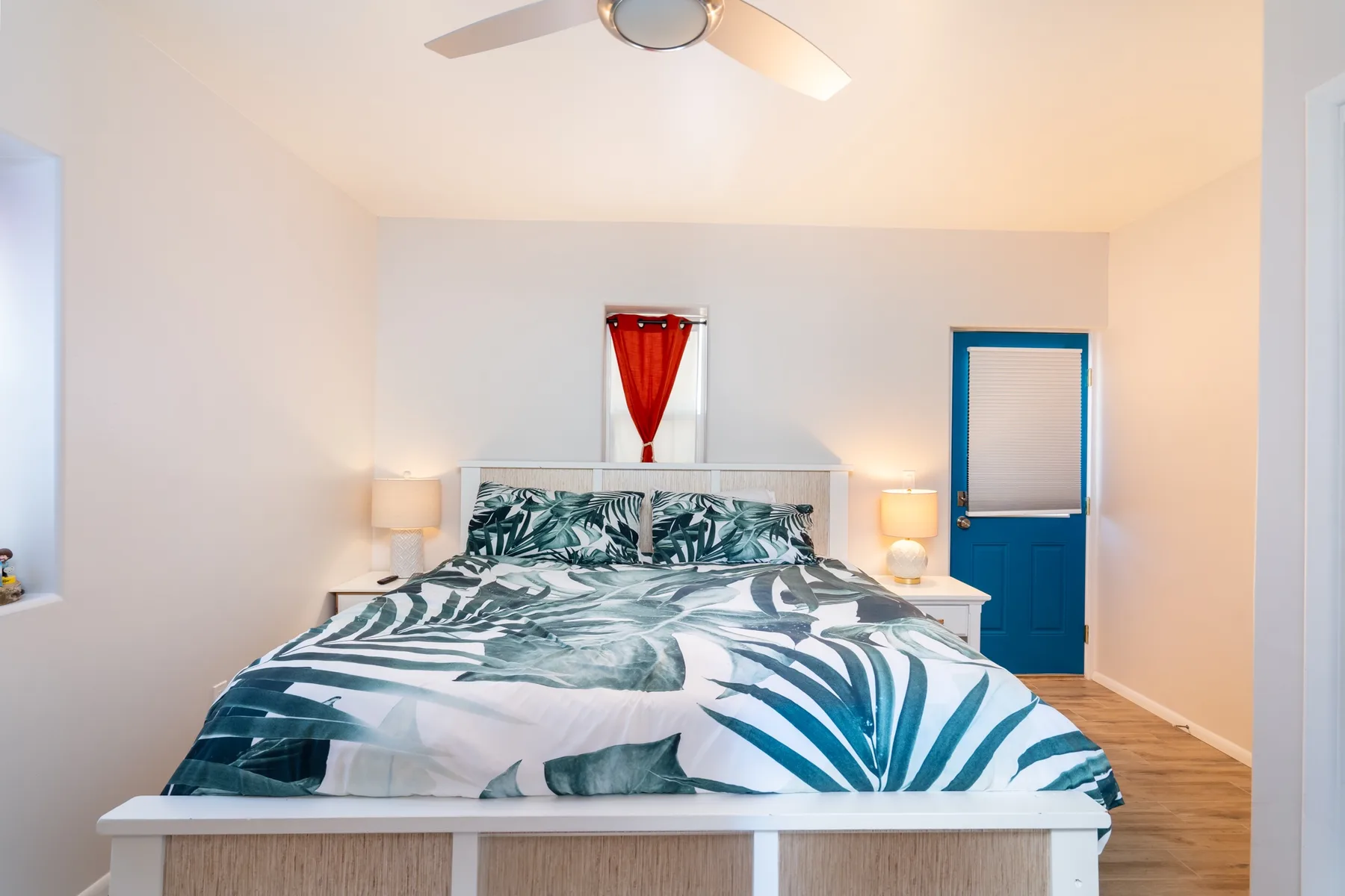 Un dormitorio con una cama cubierta con motivos de hojas tropicales verdes y blancos.