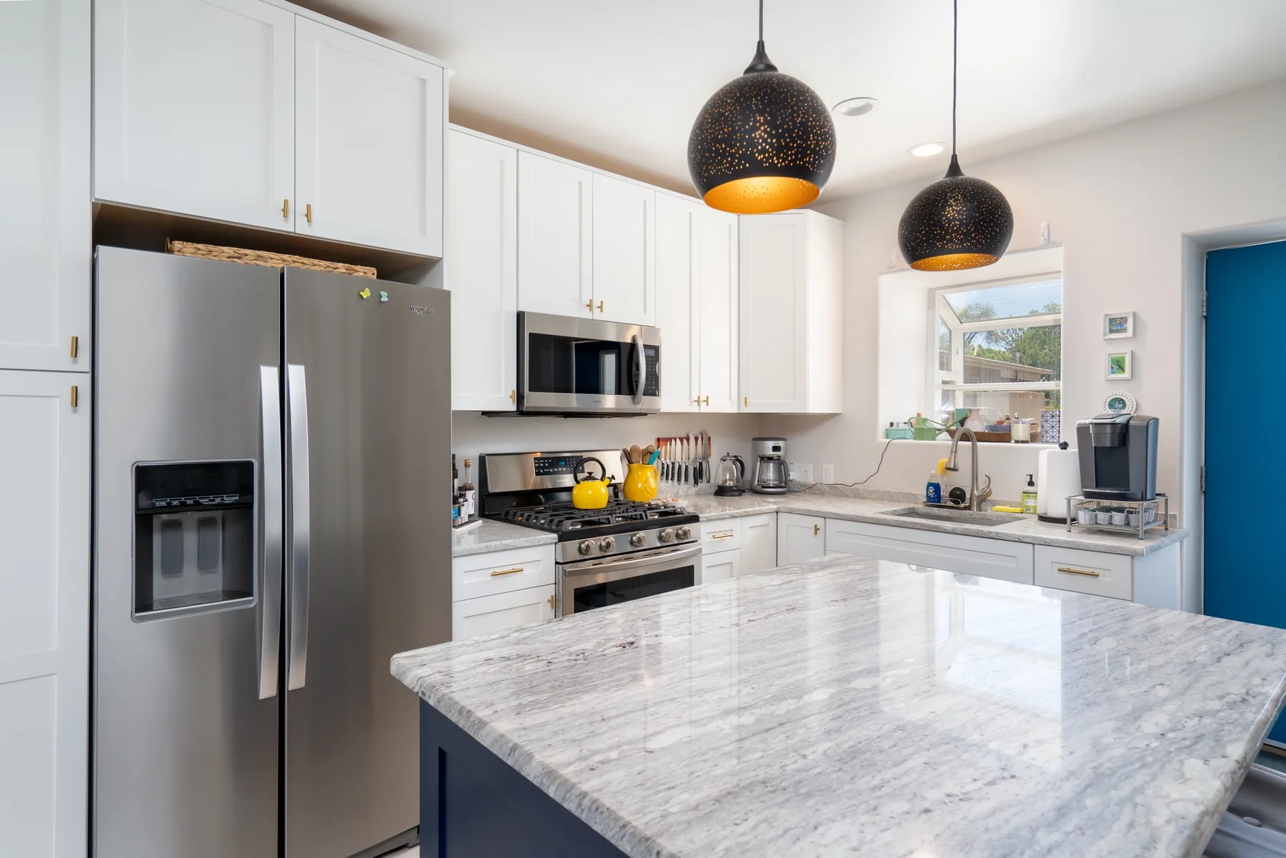 A bright kitchen with white cabinets, stainless steel appliances, and a large stone island.